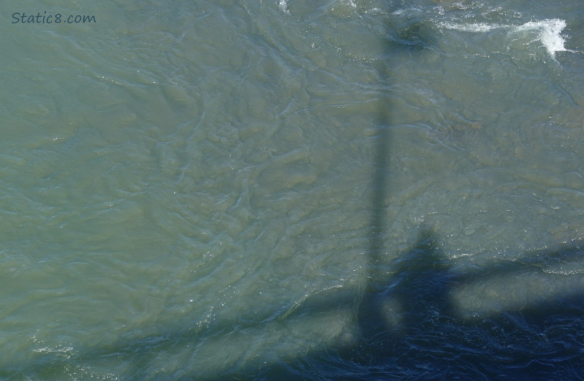 Looking down at the river water swirling, shadow of a human and railing
