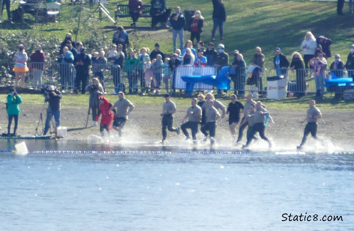 group of people running into the water, more people watching from the beach