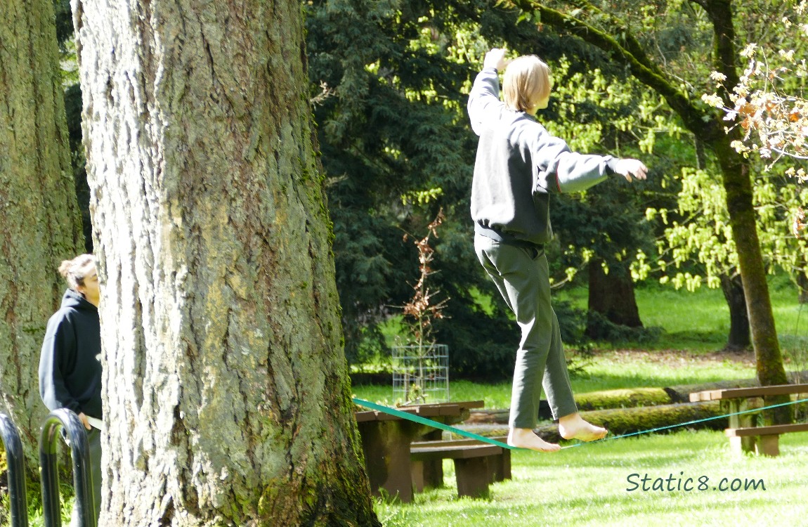 A person balancing on a low tightrope, another person looking on