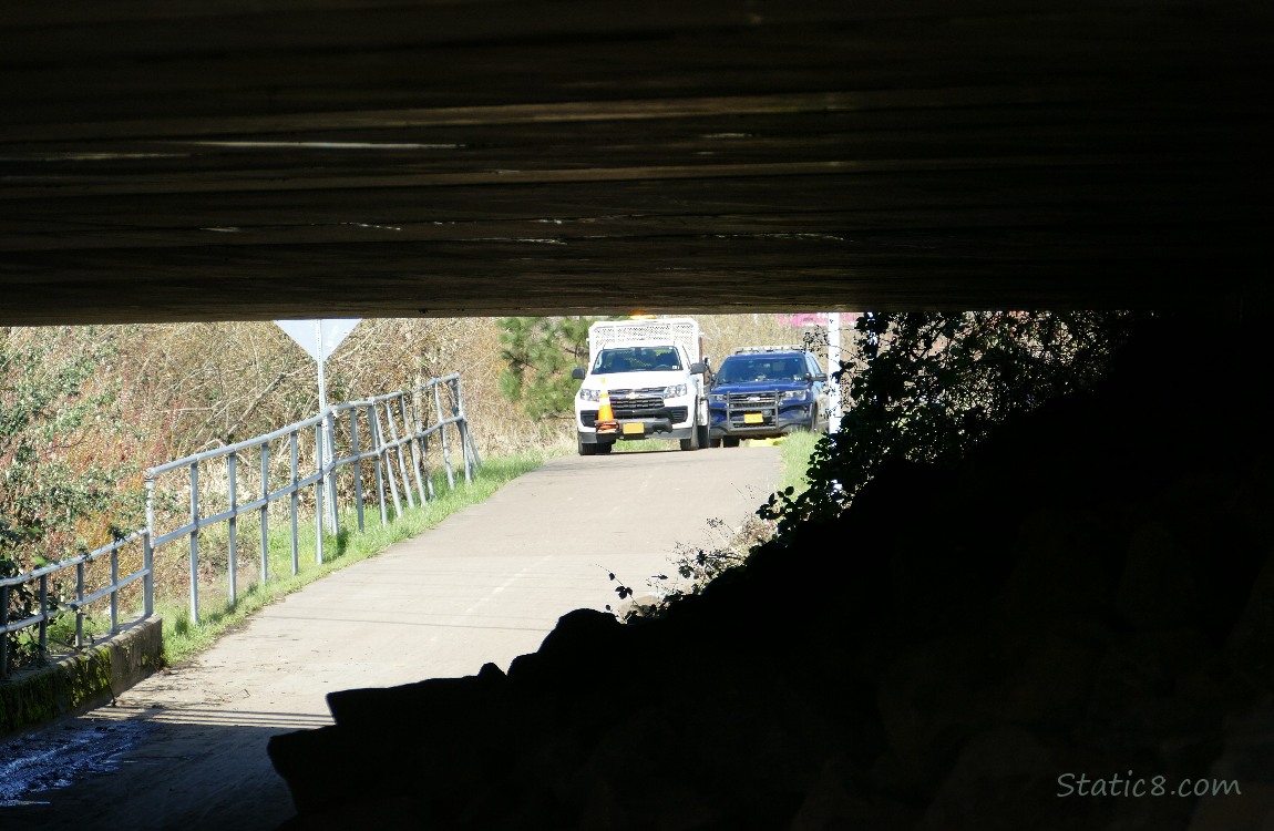 Trucks on the bike path, looking from under a dark bridge
