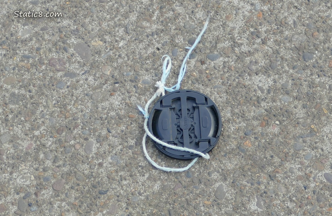 Lens cap lying on the sidewalk with a broken string