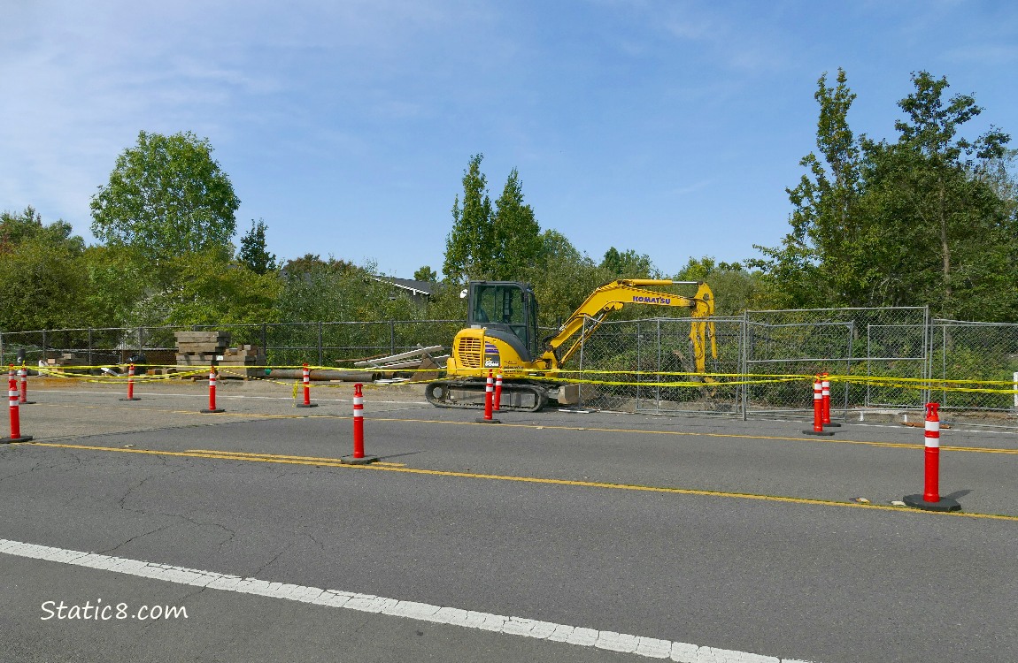 Digging machinery on a street with traffic cones and warning tape