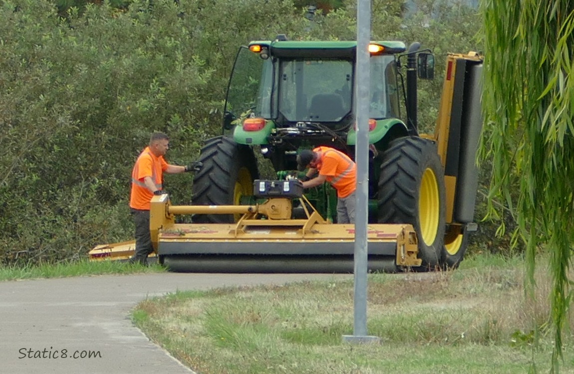 Two men looking at a tractor mower stopped on the bike path